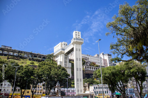 Colorful urban scene in Salvador, Bahia, Brazil, featuring the iconic Lacerda Elevator connecting the lower city to the historic upper city with traditional colonial buildings, a sunny blue sky
