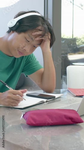 Vertical video: Placing phone on notebook, teen writing and checking phone during studying at table