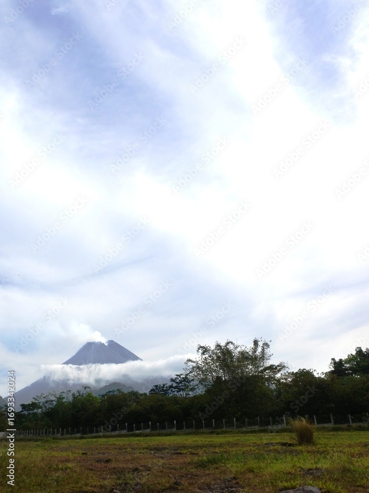 Obraz premium Beautiful view of the still active mount Merapi at Yogyakarta, Indonesia in the morning with white clouds surrounding it