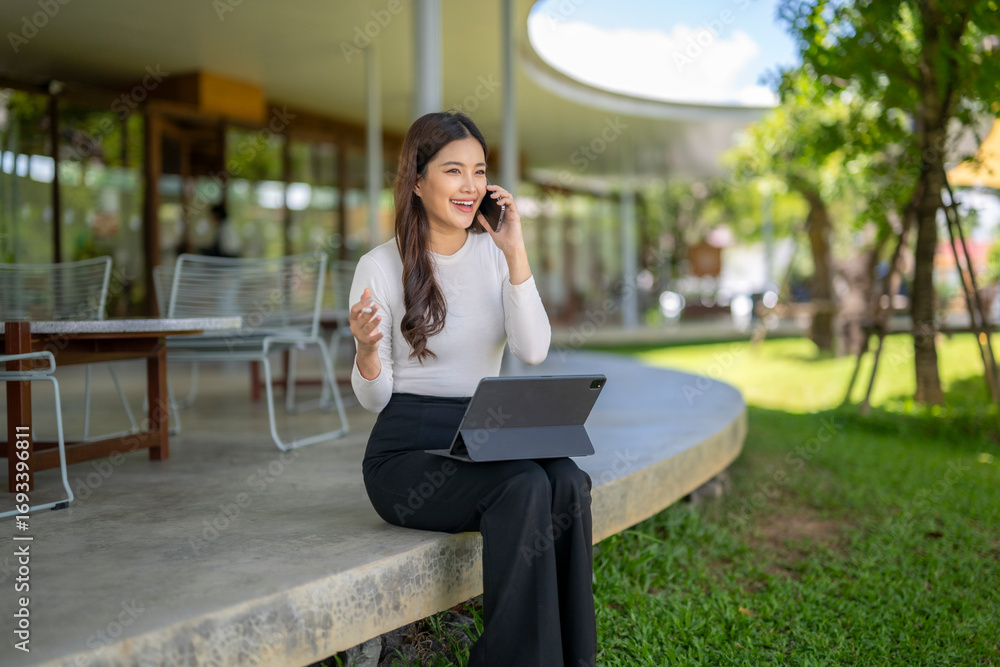 Fototapeta premium Businesswoman working remotely using tablet and talking on phone outdoors