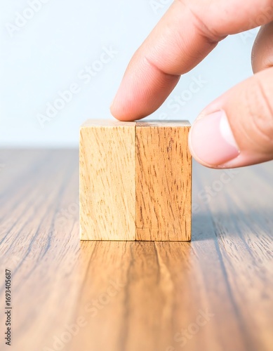 A hand gently touches a light-brown wooden block