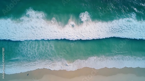 Aerial top-down view of turquoise ocean waves breaking on a sandy beach shore