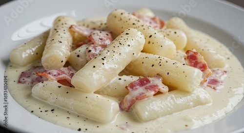 Food shot of rice cakesgaraetteok with cream sauce and bacon on a white plate