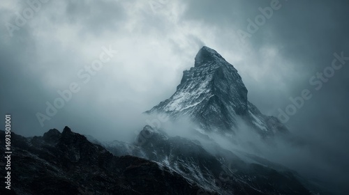 Dark atmospheric surreal landscape with towering rocky mountain peak covered in snow and surrounded by low gray clouds in gloomy overcast sky creating a mysterious and dramatic surrealist wilderness s