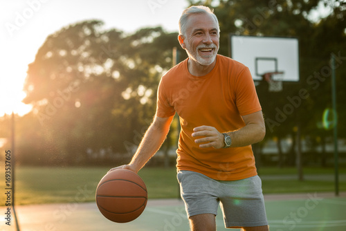 Fototapeta Naklejka Na Ścianę i Meble -  Active senior man happily playing basketball on an outdoor court