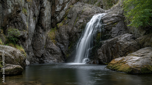 Waterfall cascading into a dark pool surrounded by rocky cliffs and green vegetation