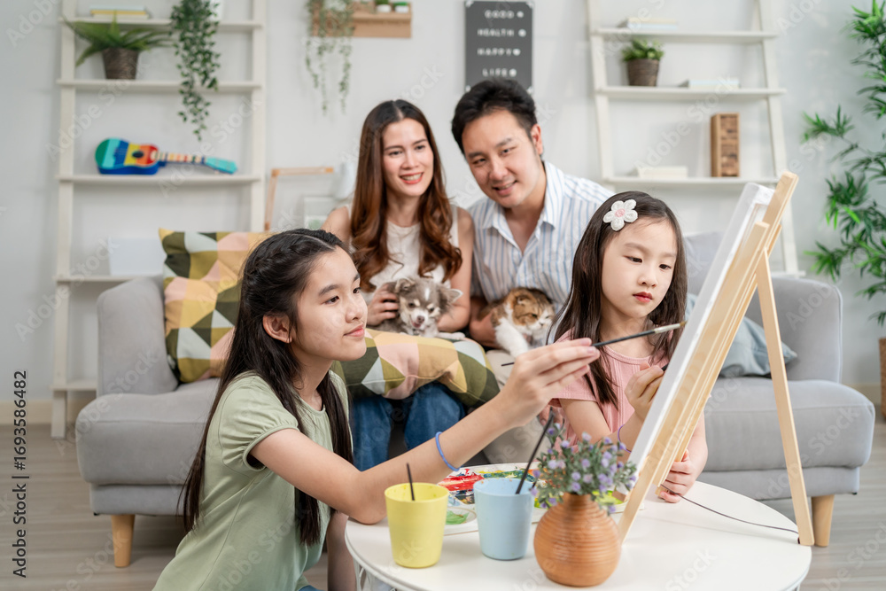 Obraz premium Asian young daughters enjoy painting on board with their parents at home. 