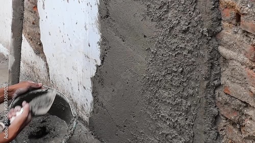 Construction worker applying wet cement plaster on wall surface during building repair and renovation