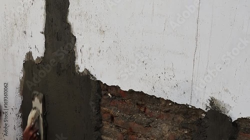 Construction worker applying wet cement plaster on wall surface during building repair and renovation