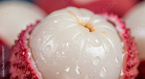 Close-up of a fresh peeled lychee fruit with water drops and a seed on a soft blurry red background, appearing refreshing.
