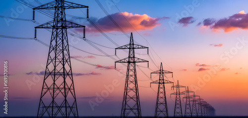 High-voltage power transmission towers and electric lines stretching across horizon under colorful sunset sky background