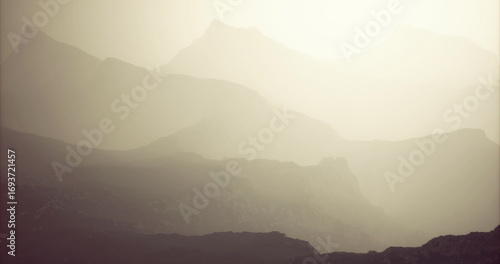 Layers of mountains fade into the distance under a soft mist during dawn. The gentle light enhances the contours, creating a serene and tranquil atmosphere in nature.