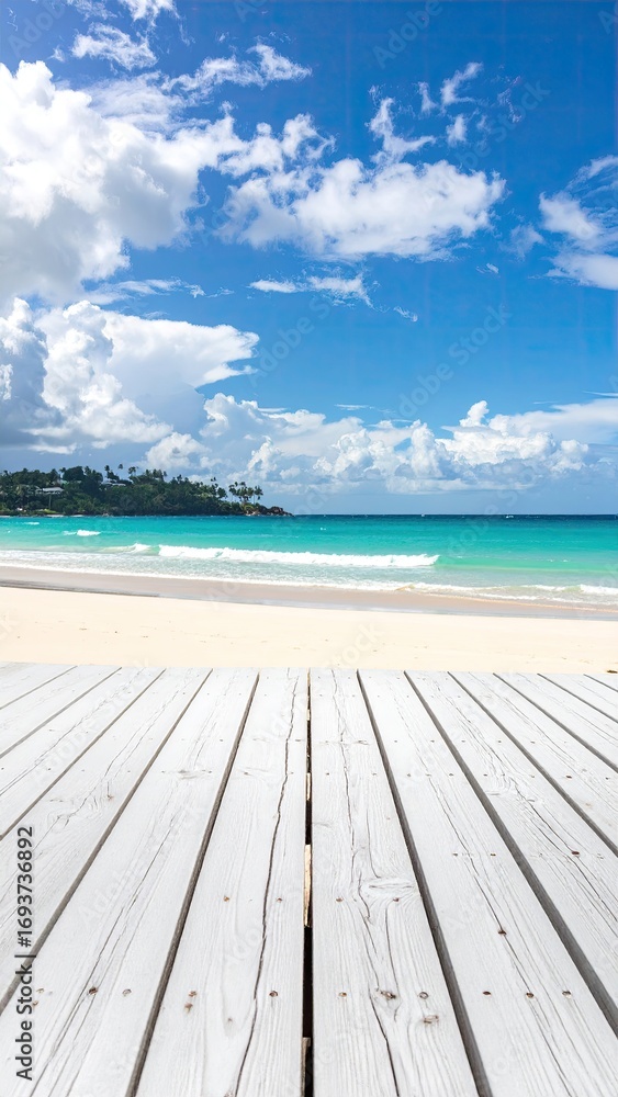 Fototapeta premium White wooden deck overlooking a tropical beach. Bright blue sky, fluffy white clouds, turquoise water, and sandy shore. Perspective is from the deck's surface, looking out towards the ocean