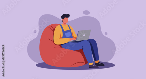 Young man enjoying flexible remote work from home, typing on laptop while relaxing on a comfortable bean bag chair. Modern digital lifestyle concept.