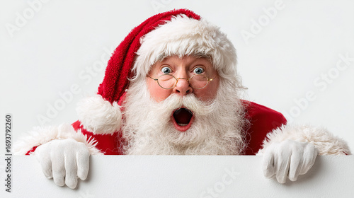 Astonished Santa Claus peeking over blank surface ready for your holiday message or promotion, festive and fun