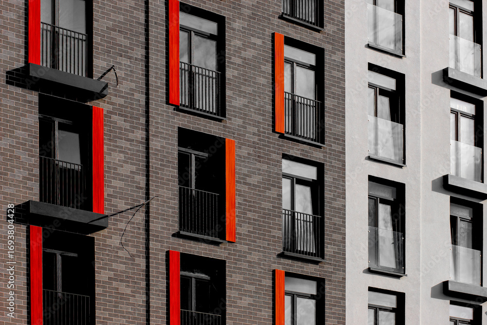Obraz premium Modern apartment facade with brick walls, black-framed windows, and striking vertical red and orange