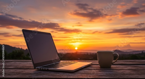 Laptop and coffee cup on wooden table at sunrise with vibrant sky and clouds