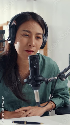 Vertical Screen : Asia girl influencer use microphone wear headphone record content with smart phone online audience listen at house. Student female podcaster make audio podcast from her home studio.