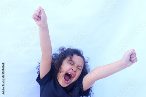 Portrait of an Asian girl who has just woken up with both hands raised while yawning widely.