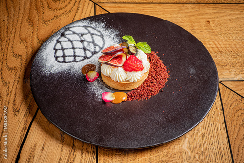 Schilderij op canvas A stunning black plate holds a lavish dessert topped with figs and strawberries