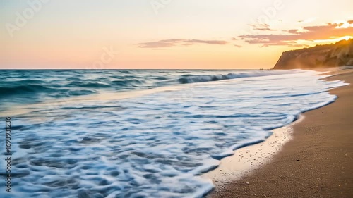 Beach scene showing ocean waves at sunset with a sandy shore and bluff on right