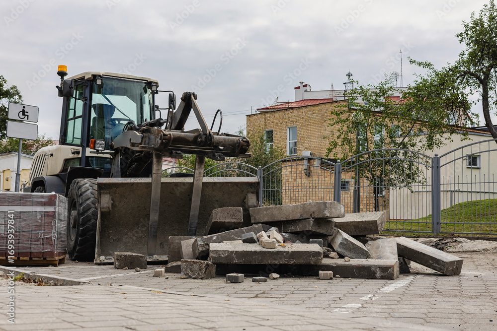 Fototapeta premium Construction machinery moves large concrete slabs in urban renovation effort during cloudy day
