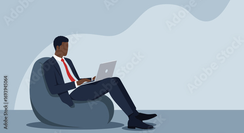 African American businessman works remotely on a laptop from a comfortable beanbag chair. Illustrates modern work flexibility and productivity.
