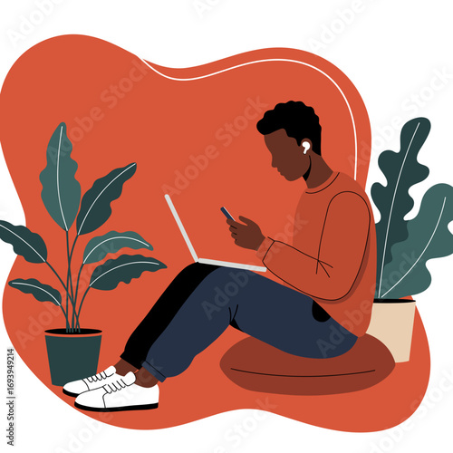 Young Black man casually working or studying from home, using a laptop and smartphone with earbuds. Illustrates modern remote lifestyle, productivity, and digital connectivity.