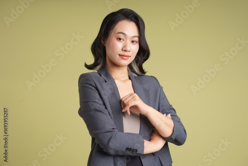 Professional young woman poses confidently in a suit against a green background in a studio
