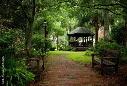 Serene park scene featuring a red brick path, benches, and a gazebo amidst lush greenery, flowers, and trees in soft, natural light
