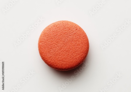 Isolated orange macaron cookie on white. Slightly textured with a subtle shadow, creating a clean food shot
