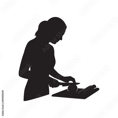 Silhouette of a woman preparing food on a cutting board with a knife.