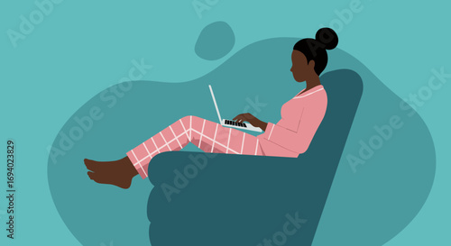 Young African American woman in pajamas working remotely on her laptop at home, embodying comfort and modern flexible work-life balance.