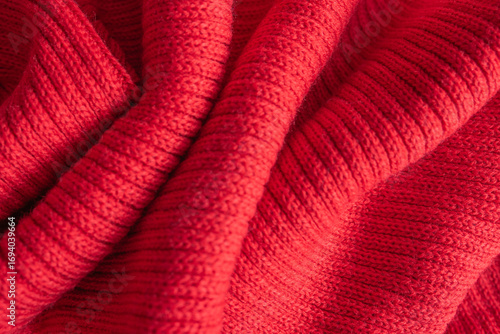 Texture of a knitted red sweater folded in a swirling pattern.
