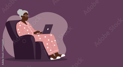 Elderly African American woman in pink polka-dot pajamas relaxing in a recliner, using a laptop at home. Represents senior technology use, online learning, or a comfortable digital lifestyle.