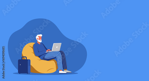 Elderly man relaxing on a bean bag chair, working remotely on his laptop. Suitcase nearby suggests digital nomad lifestyle and travel.