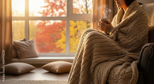 A woman is sitting in a chair with a mug of coffee in her hand, fall, autumn. The mug is steaming and the woman is wearing a sweater