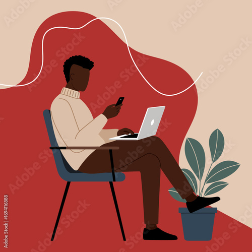 Young Black man multitasking, working remotely on his laptop while checking his phone. Represents modern productivity and digital communication lifestyle.