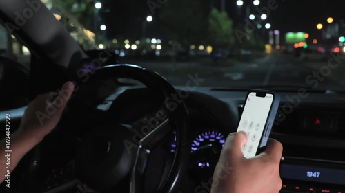 Driver using smartphone while driving car at night in city street traffic