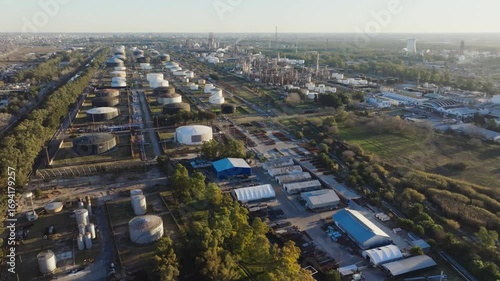 Drone footage of oil and gas refinery with storage tanks and processing facilities in Argentina at sunset.