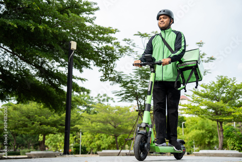 Rider food delivery man wearing green uniform and helmet ride the EV scooter delivery food service to customer. Happy delivery man with green backpack shipping of goods to customers by scooter