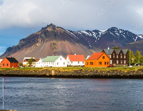 Colorful houses line a riverfront, mountains rise behind