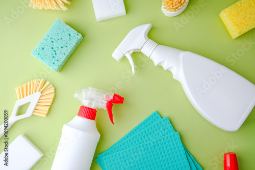 Cleaning supplies, sponges and brushes scattered on green background for household chores and tidy up