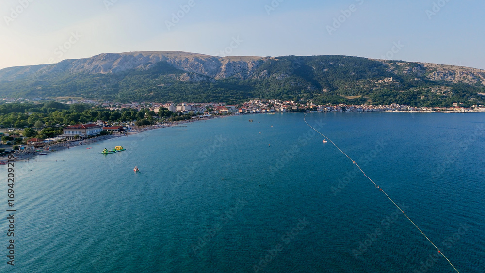 Naklejka premium Baska Beach and Coastline With Clear Turquoise Water, Marina Boats, City Street, Sunny Summer Sunset Aerial View on Krk Island, Croatia Adriatic Sea, Vela Plaza Beach, Mountains and Campsite Cityscape