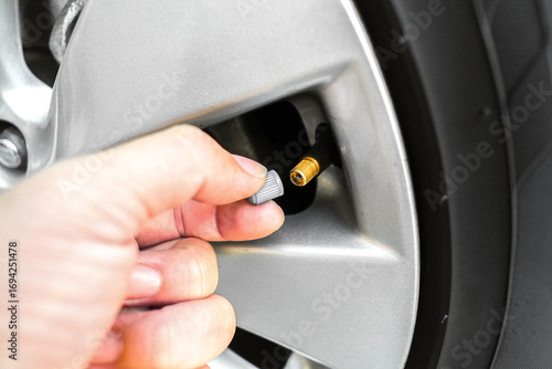 Hand opening tire valve cap on car wheel rim, close up of vehicle air valve for checking tire pressure, automotive maintenance and safety concept for inflation, air check and car care
