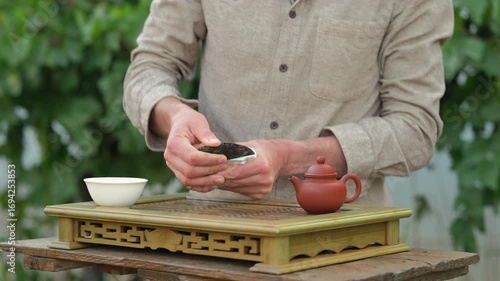 Close up shot of a man breaking off a piece of tea from a tea brick, man standing behind a chaban, clay tea pot on the side