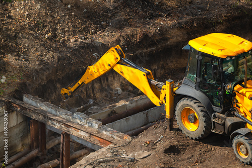 Excavator bucket operates as crane for extraction and replacement of water pipes at construction site during repair works of public utilities