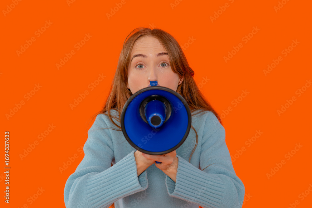 Fototapeta premium Young woman holds megaphone to convey an important message against vibrant orange backdrop during an energetic gathering in the afternoon