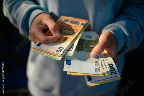 Person holding euro banknotes in hands, counting money outdoors. Close-up view of 50, 100, and 200 euro bills