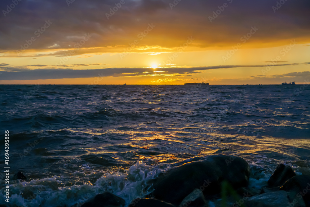 Naklejka premium Golden Sunset over the Ocean with Rocks in the Foreground